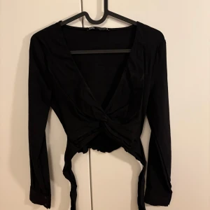 Svart långärmad topp med knyt på ryggen - Snygg svart långärmad topp med v-ringning och knytning baktill. Perfekt för en stilren look.