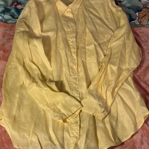 Gul linneskjorta - Säljer en solgul skjorta i linne med klassisk krage och knappar framtill. Perfekt för varma dagar med sin lätta och luftiga känsla. Skjortan har långa ärmar och en bröstficka för extra stil och funktionalitet.