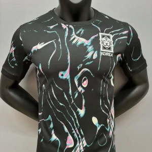 Svart fotbollströja med mönster - Snygg svart fotbollströja med unikt mönster i rosa, blått och vitt. Tröjan har korta ärmar och ett tryckt emblem på bröstet. Perfekt för sportiga tillfällen eller som en cool vardagslook.