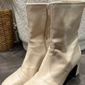 Beige boots med dragkedja - Snygga beige boots med dragkedja och klack. Tillverkade i syntetmaterial med en stilren design. Perfekta för att ge en elegant touch till din outfit.