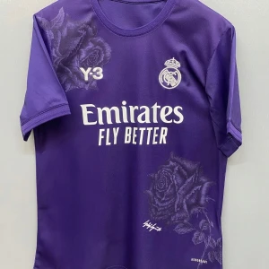  Real Madrid fotbollströja från XS/S/M/L - Snygg lila fotbollströja från Real Madrid med korta ärmar. Tröjan har ett elegant ros-mönster och vit text med 'Emirates Fly Better'. Perfekt för fans som vill sticka ut på läktaren!