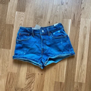 Blå jeansshorts från Levi's - Snygga blå jeansshorts från Levi's modell 501. De har en klassisk design med fem fickor och knappgylf. Perfekta för en avslappnad stil. Dom är helt nya men lapparna på bilden är inte kvar 