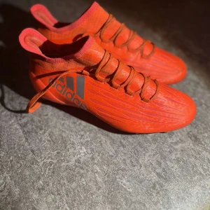 Röda fotbollsskor från Adidas - Snygga röda fotbollsskor från Adidas med snörning och dobbar för optimalt grepp på planen. Perfekta för fotbollsspelare som vill sticka ut med stil.