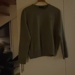 Grå tröja från Ralph Lauren originalpri 2000 - Säljer en stilren grå tröja från Ralph Lauren med rund hals och långärmad design. Perfekt för en avslappnad och klassisk look. Tröjan har en liten broderad logotyp på bröstet. Storlek xl passa M