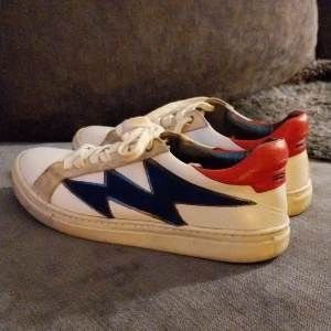 Vita sneakers från Zadig & Voltaire - Snygga vita sneakers från Zadig & Voltaire med blå detaljer på sidorna och röd häl. Skorna har snörning och en klassisk design som passar perfekt för en avslappnad stil. Små i storlek, mer som 36.