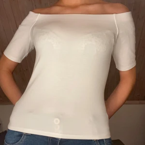 Vit offshoulder topp - Snygg vit offshoulder topp med korta ärmar. Perfekt för en stilren och enkel look. Passar bra till jeans eller kjol för en avslappnad stil.