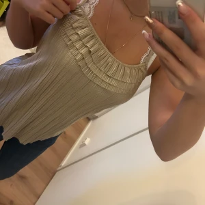 linne med spetsdetaljer - Snygg topp med spetsdetaljer på axelbanden. Leotarderna har en lös passform och ett veckat mönster på framsidan, vilket ger den en stilren look. Perfekt för varma sommardagar.