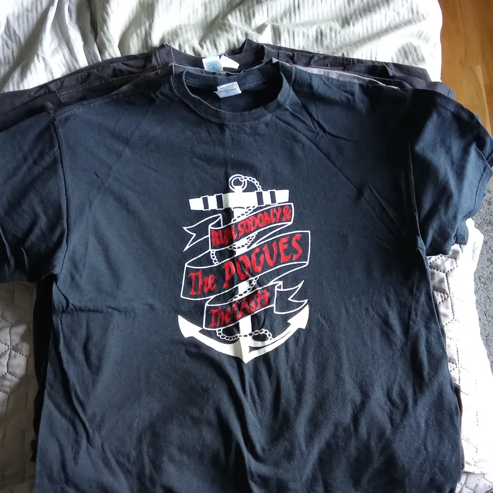 Säljer en svart t-shirt med tryck i grönt och rött. T-shirten har ett ankarmotiv och texten 'Rum Sodomy & The Lash'. Perfekt för fans av the pogues. T-paidat.
