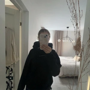 Svart hoodie med tryck - Säljer en svart hoodie med ett stort vitt tryck på ryggen. Hoodien har en klassisk design med luva och långa ärmar. Perfekt för en avslappnad stil.