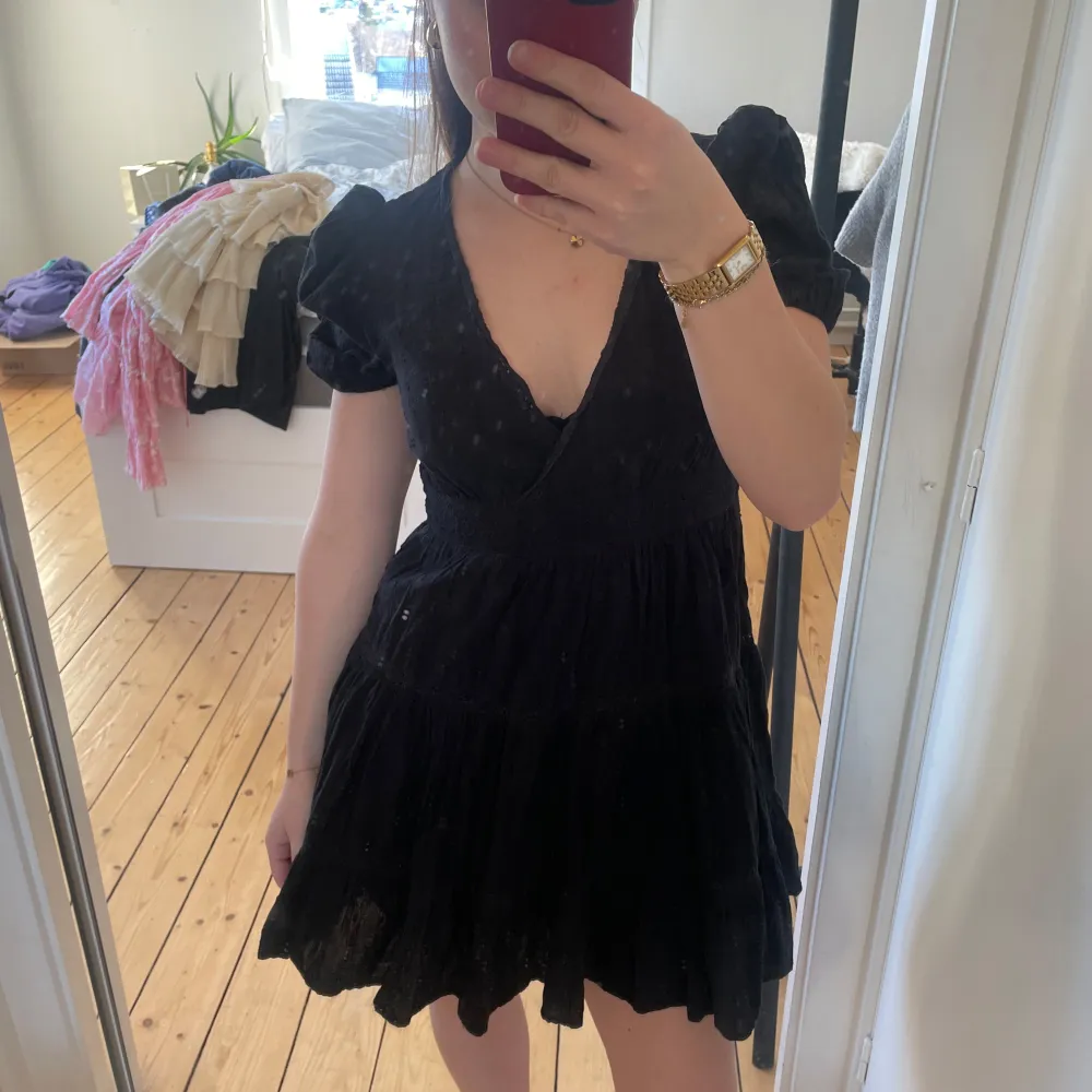Snygg svart omlottklänning med kort puffärm och v-ringning. Klänningen har ett subtilt mönster och volangdetaljer som ger en romantisk touch. Perfekt för en stilfull look.. Mekot.