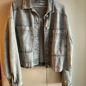 Ljusblå jeansjacka från Gina tricot  - Snygg grå jeansjacka med knappar och stora fickor framtill. Jackan har en klassisk krage och långa ärmar. Perfekt för en avslappnad stil.