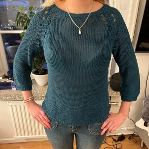 Petrolblå stickad tröja - Säljer en snygg petrolblå (blågrön) stickad tröja med trekvartsärmar och dekorativa hål längs axlarna. Tröjan har en rund halsringning och ribbade kanter för en bekväm passform. Färgen syns bäst på de 2 sista bilderna. Tröjan har 2 sömmar som sticker ut som man kan se på sista bilden, men det går att fixa lätt genom att trä sömmen genom en nål och sticka igenom nålen i tröjan!!💗