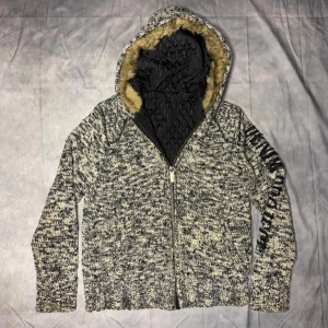 Stickad Cardigan/Jacka med päls - Säljer nu en riktigt trändig och eftertraktad cardigan/jacka med pälsfodrad huva och dragkedja. Jackan har ett stickat mönster och textdetalj på ärmen. Perfekt för kyliga dagar som nu. Liten defekt inuti syns ej på utsidan.