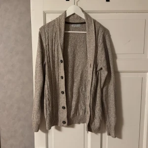 Beige stickad cardigan - Säljer en stilren beige kofta från Avenue med kabelstickat mönster. Koftan har långa ärmar och knappar framtill, perfekt för kyliga dagar. Den är mjuk och bekväm att bära. Storlek M.