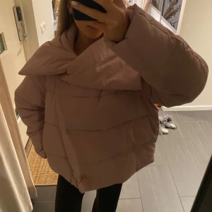 Rosa pufferjacka - Säljer en snygg rosa pufferjacka med större krage och knappar framtill. Jackan har en oversized passform för mig som brukar bära S i jackor. 