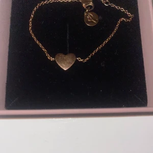 Guldarmband med hjärta från Edblad - Elegant guldarmband från Edblad med ett hjärta dekorerat med små glittrande stenar. Perfekt för att ge en touch av glamour till din outfit. Armbandet har en justerbar kedja och kommer i en fin presentask.