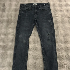 Grå jeansbyxor med slitningar - Snygga grå jeansbyxor med en cool slitning på framsidan. De har en klassisk femficksdesign och en bekväm passform. Perfekta för en avslappnad stil.