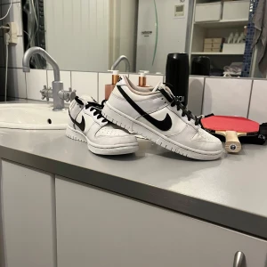 Nike Dunk i vitt och svart - Snygga Nike Dunk sneakers i vitt med svarta detaljer. Skorna har en klassisk design med snörning och en bekväm passform. Perfekta för en stilren look, priset kan diskuteras 