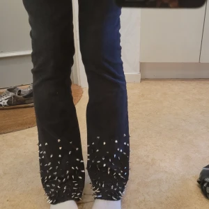 Svarta jeans med nitar från Custommade - Snygga svarta jeans från Custommade med coola nitar längst ner på benen. De har en tight passform och är lågmidjade, vilket ger en trendig look. Perfekta för att ge din outfit en edgy touch. Jeansen är i bootcut-stil. 