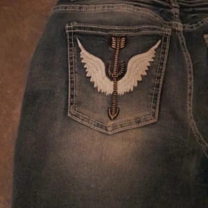 Blå jeans med broderade fickor - Snygga blå jeans med bootcut-stil och unika broderade detaljer på bakfickorna. Jeansen har en klassisk femficksdesign och en bekväm passform. Perfekta för en avslappnad look med en twist.