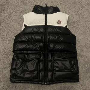 Svart och vit dunväst från Moncler - Pris kan diskuteras! Äkta!! Allt med kommer, Tag m.m.Limited Edition dunväst från Moncler. Västen har en avtagbar huva med Moncler-logga. Perfekt för till våren! Skick 8,5/10 🥂