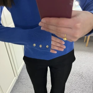 Blå tröja med guldknappar från Holly & Whyte - Snygg blå tröja från Holly & Whyte med långa ärmar och dekorativa guldknappar vid ärmsluten. Tröjan har två små defekter (se bild 4&5) därav har jag sänkt priset, original pris 399kr. Den säljs inte längre heller💕