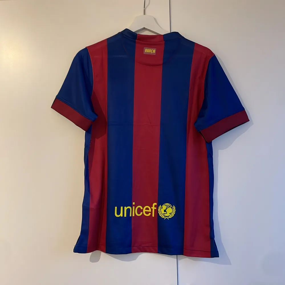 Säljer en officiell FC Barcelona fotbollströja från Nike i blått och rött med klubbens emblem och Qatar Airways-logga. Tröjan är kortärmad och har Dri-FIT-teknologi för optimal komfort. Perfekt för alla Barça-fans! 2014/15 hemma tröja 💙❤️. T-paidat.
