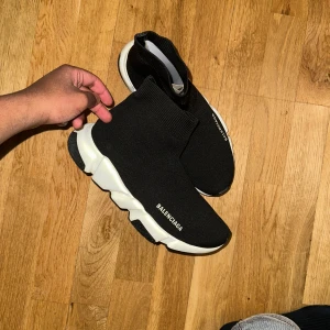 Svarta sneakers från Balenciaga - Snygga svarta sneakers från Balenciaga med en strumpliknande design och vit sula. Skorna har en modern och stilren look, perfekt för en trendig outfit.