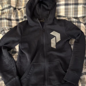 Mörkblå hoodie från Peak Performance - Säljer en svart hoodie från Peak Performance med dragkedja och en stilren logga på bröstet. Perfekt för kyliga dagar med sin mjuka insida och praktiska fickor. Huvan ger extra värme och stil. Knappt använd och i fint skick. Passar xs å s. Säljer mer plagg på min Vinted @astrid450!! 