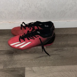 Röda fotbollsskor från Adidas jätte sköna att lira med - Snygga röda fotbollsskor från Adidas med svarta och vita detaljer. Skorna har snörning och är perfekta för fotbollsplanen. De har en sportig design med klassiska ränder på sidan.