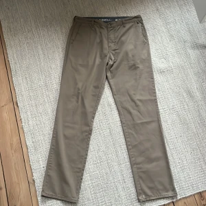 Beige chinos från Billabong - Snygga beige chinos från Billabong i storlek W32. De har en rak passform och klassisk design med knappar och dragkedja. Perfekta för en stilren look.
