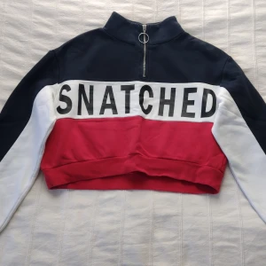 Flerfärgad croppad tröja med text - Säljer en cool croppad tröja med texten 'SNATCHED'. Tröjan har en dragkedja framtill och är i färgerna blå, vit och röd. Mjuk och skön. Det vita tyget är en aning nopprigt. Storlek S.