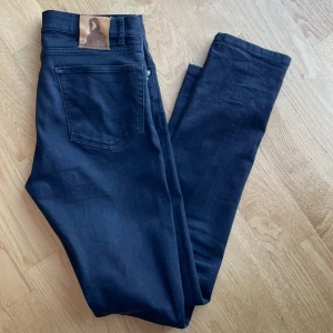 Svarta jeans från Velour - Snygga svarta jeans från Velour med klassisk femficksdesign och knappgylf. Perfekta för en stilren look. Märkesdetalj på bakfickan ger en extra touch.