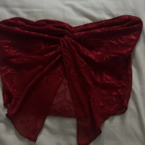 Röd axelbandslös topp med rosdetaljer - Snygg röd axelbandslös topp med vackra rosdetaljer. Perfekt för en kväll ute eller en speciell tillställning. Toppen har en elegant drapering framtill som ger en unik look.