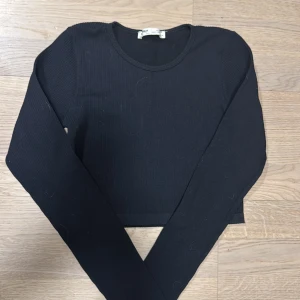 Svart ribbad tröja från Pull&Bear - Säljer en stilren svart ribbad tröja från Pull&Bear. Tröjan har en croppad design och långa ärmar, perfekt för en trendig look. Passar utmärkt till både jeans och kjol. Hör av dig vid intresse!