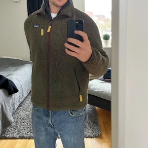 Olivgrön fleecejacka från Patagonia - Säljer en olivgrön fleecejacka från Patagonia med dragkedja och hög krage. Perfekt för kyliga dagar!