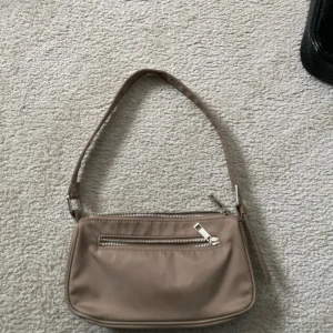 Beige axelväska med dragkedja - Snygg beige axelväska i syntetmaterial med en praktisk dragkedja framtill. Perfekt för att bära med sig det viktigaste på ett stilrent sätt.