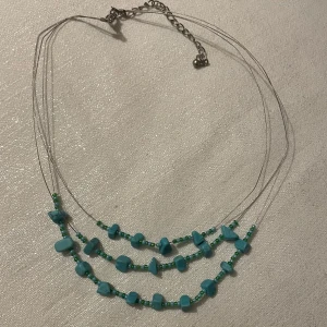 Turkost halsband med stenar - Charmigt halsband med flera rader av turkosa stenar och små gröna pärlor. Halsbandet har en justerbar kedja för perfekt passform. Perfekt för att ge en färgklick till din outfit.