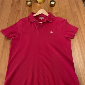 Burberry Piké - Pikétröja från den fina märket burberry i en härligt röd färg. Tröjan är i fint skick och har inga deffekter! Tröjan är i storlek L men passar M/L skulle jag säga. Tröjan är köpt för 2000 cirka ett år sedan. Vid fler frågor är det bara att kontakta!