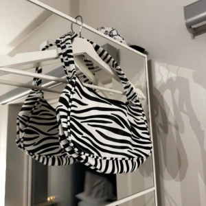 Zebramönstrad axelväska - Snygg zebramönstrad axelväska med dragkedja. Perfekt för att ge din outfit en djärv touch. Väskan har ett bekvämt handtag och är lätt att bära med sig.