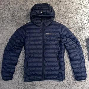 Blå dunjacka Peak Performance - Säljer en snygg blå dunjacka från Peak Performance. Jackan har en quiltad design med dragkedja och huva, perfekt för kyliga dagar. 
