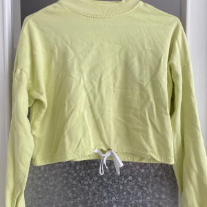 Gul croppad tröja - Säljer en ljusgul croppad tröja med långa ärmar. Tröjan har en ribbad krage och en knytning i nederkanten. Perfekt för vår och sommar! 🌼