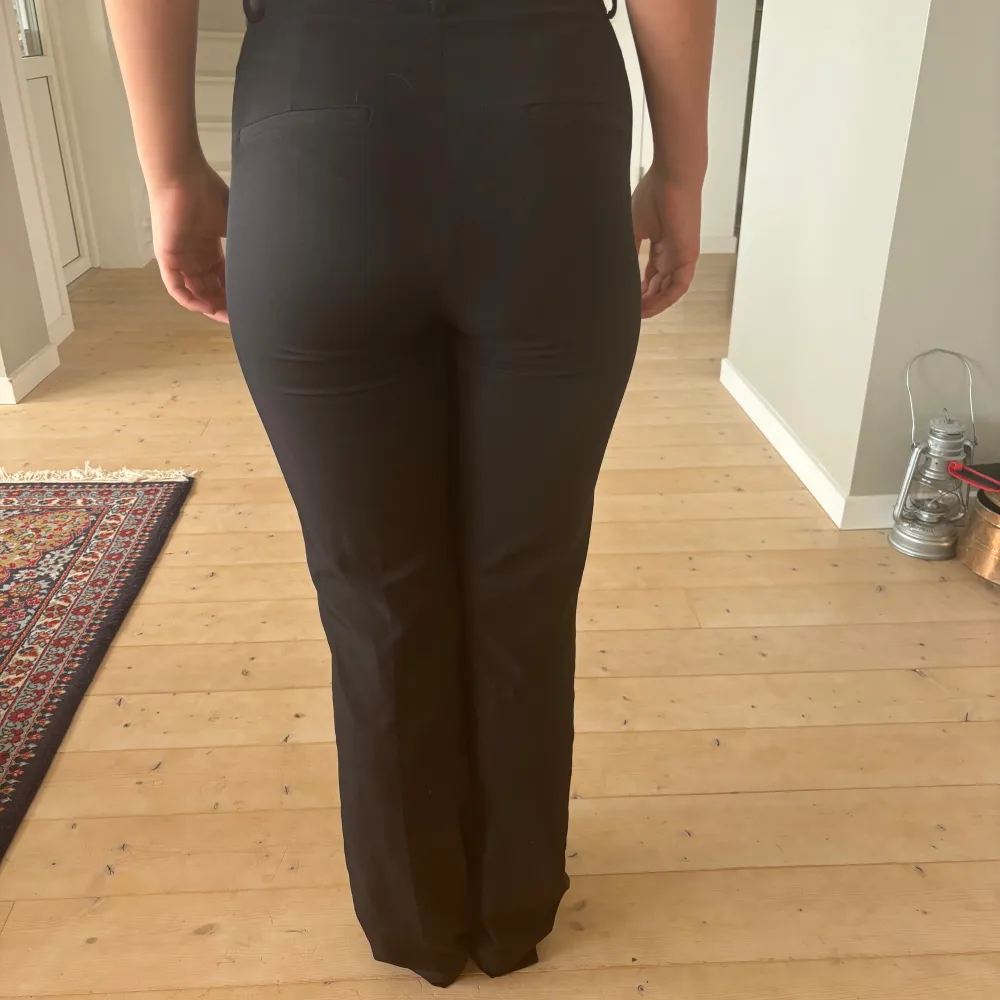 Säljer ett par svarta kostymbyxor i storlek 34.  Byxorna är mid-highwaist och har en bootcut passform.  Materialet känns bekvämt och ser stilrent ut. Min kompis på bilden är 160cm lång men de är lite långa för henne. Köpta för ca 400kr och säljer för 150kr. Köparen står för frakten!!. Jeans & Byxor.