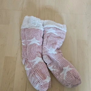 Mysiga rosa och vita strumpor - Säljer ett par supermysiga rosa strumpor med vita stjärnmönster. De är fluffiga och perfekta för att hålla fötterna varma under kalla vinterdagar. Strumporna har en mjuk insida som känns som att gå på moln. Perfekta för att mysa hemma eller som en söt present!