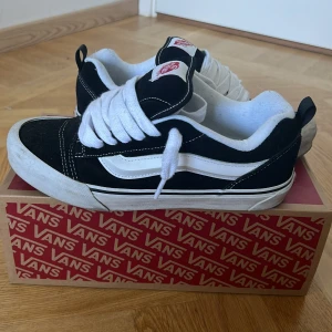 Vans Knu Skool - Säljer ett par svarta Vans sneakers i storlek 42.5 för herrar. Skorna är i bra skick med vit sula och vita snören. De har den klassiska Vans-loggan på sidan och är perfekta för vardagsbruk. Kommer med originalkartong. 