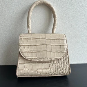 Liten handväska  - Liten helt oanvänd (prislapp kvar) handväska.  Märke: NLY accessories. Den är i en gammelrosa/beige färg. Inga fack inuti. Kan mötas i Centrala Stockholm eller frakta.