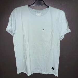 Ljusgrön t-shirt från Denim AY - Säljer en ljusgrön t-shirt från Denim AY. Den har en bröstficka med en liten knappdetalj och är gjord av mjukt bomullsmaterial. Perfekt för en avslappnad stil. T-shirten är i nyskick och har korta ärmar.