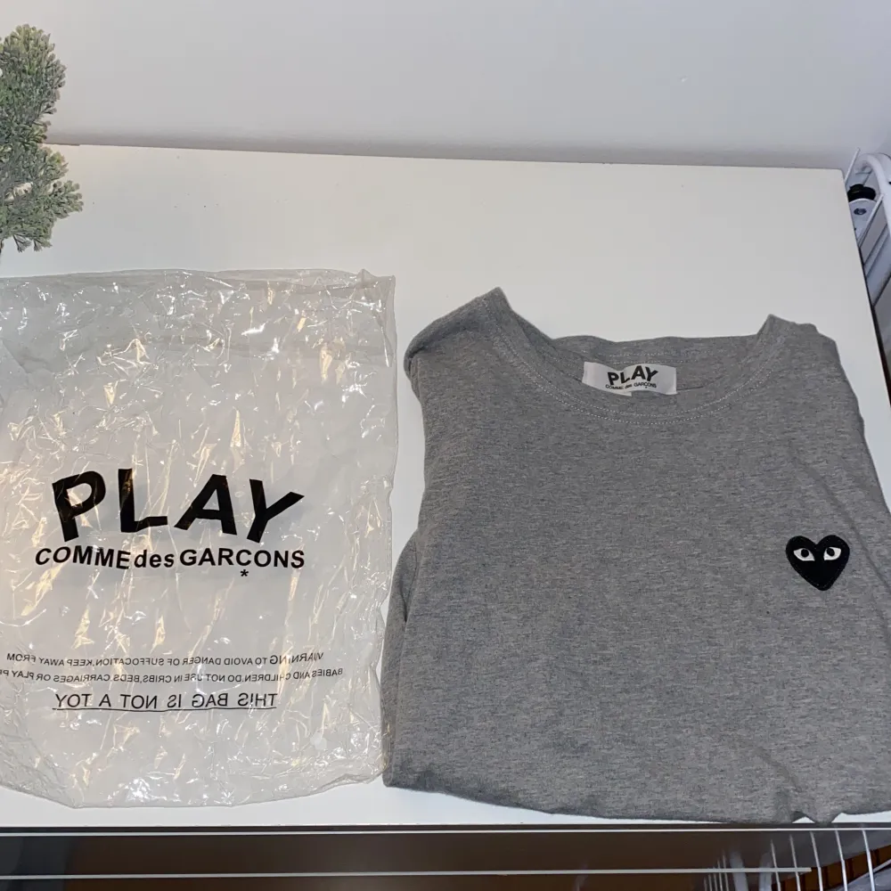 Säljer en grå t-shirt från Comme des Garçons PLAY i storlek M. T-shirten är gjord av bomull och har en normal passform. Den har korta ärmar och ett svart hjärta med ögon på bröstet samt ett större tryck med ögon längst ner. Tröjan säljs inte längre så den är limiterad. Perfekt för en casual look!. T-shirts.