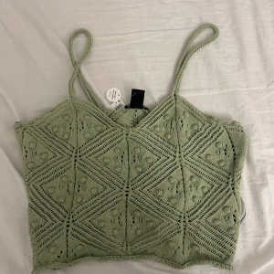Grön stickad topp från Lindex - Säljer en superfin grön stickad topp från Lindex. Den har ett snyggt mönster med små hål och geometriska former. Toppen har smala axelband och är perfekt för sommaren. Den är i nyskick och aldrig använd. Passar perfekt till både vardag och fest!