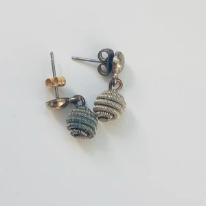 Unika örhängen med spiraldesign - Säljer ett par unika örhängen med en cool spiraldesign. De är i en mix av silver och guld färger och har en liten hängande spiralformad detalj. Perfekta för att ge din outfit en extra touch! 🌀✨